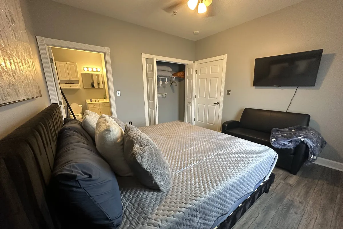 A cozy corner featuring a king-sized bed adjacent to a plush couch, a television conveniently positioned for viewing, and a bathroom door in the background. The mood is inviting and serene, suggesting options for relaxation, watching TV, or enjoying peaceful mornings with coffee.