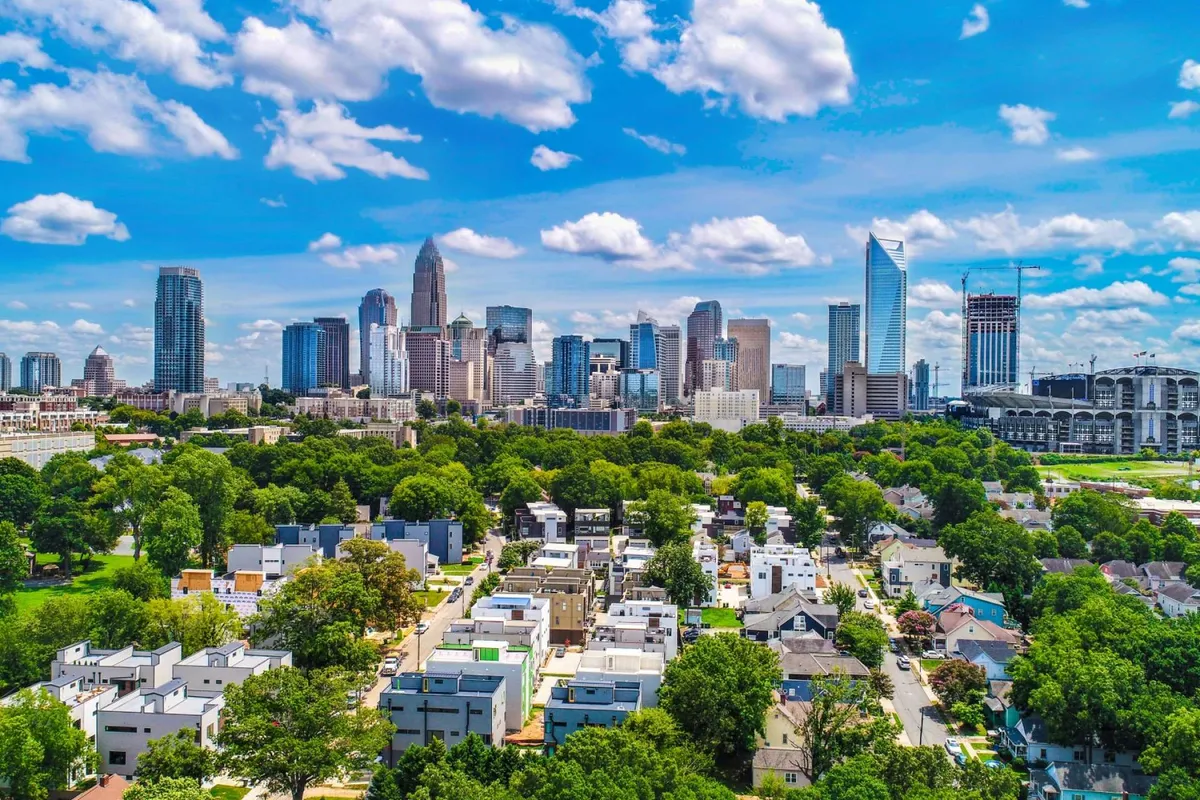 A sweeping view of Charlotte’s city skyline with green parks and residential neighborhoods in the foreground. The image captures the vibrancy of the city, hinting at urban exploration, community events, and proximity to cultural attractions, shops, and cafes.