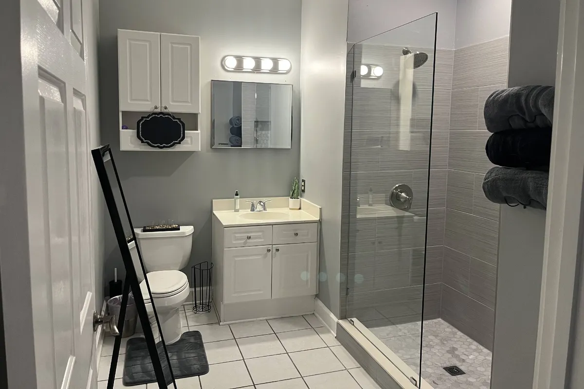 A fresh and inviting bathroom featuring a modern shower area, sleek vanity with mirror, and bright morning light. The setting is ideal for personal grooming and unwinding with a hot shower after a long day.