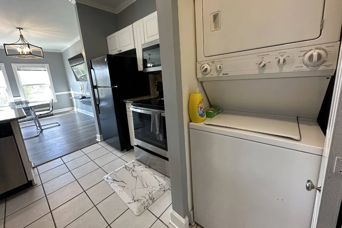 A bright, functional laundry area featuring a modern washing machine and dryer, with kitchen appliances visible nearby. The space is organized and practical, emphasizing ease for daily routines and longer stays.
