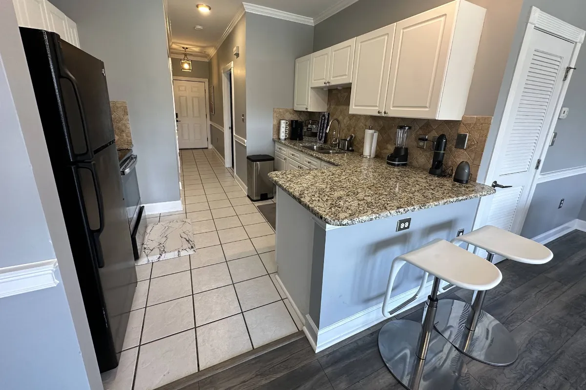 A modern kitchen space with granite countertops, sleek bar stools, and stainless steel appliances. The setup is ideal for casual dining, working remotely, or socializing in a comfortable environment.