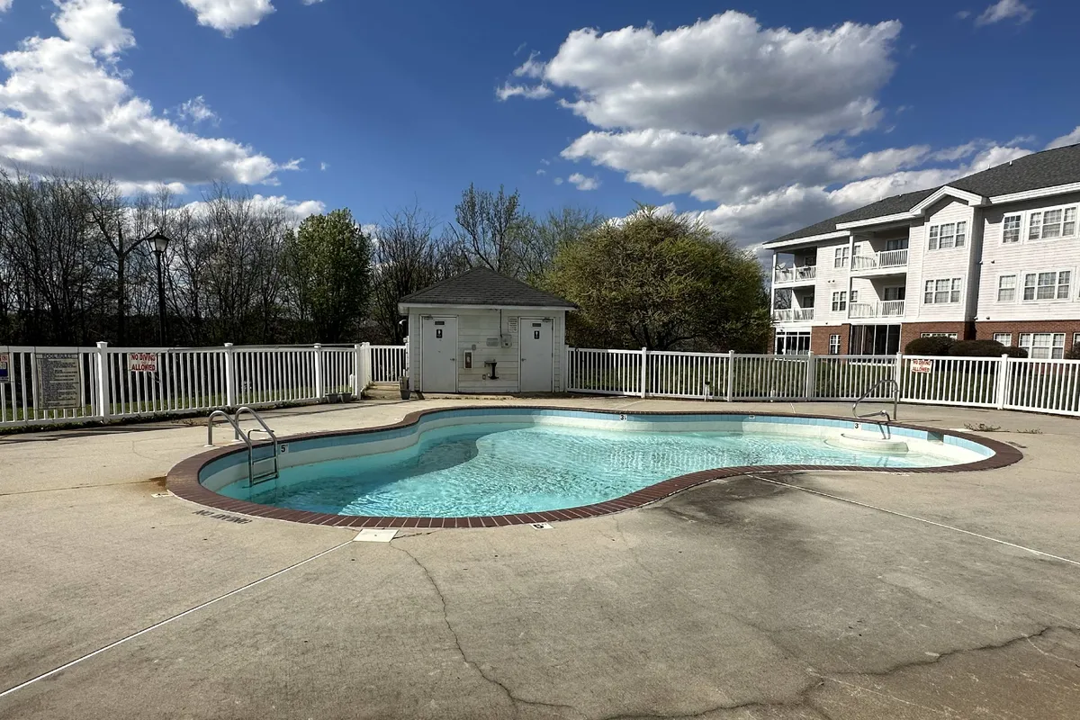 A tranquil community swimming pool surrounded by lush greenery, with a stylish pool house nearby. The poolside area invites relaxation and social gatherings, and the setting is vibrant yet serene.