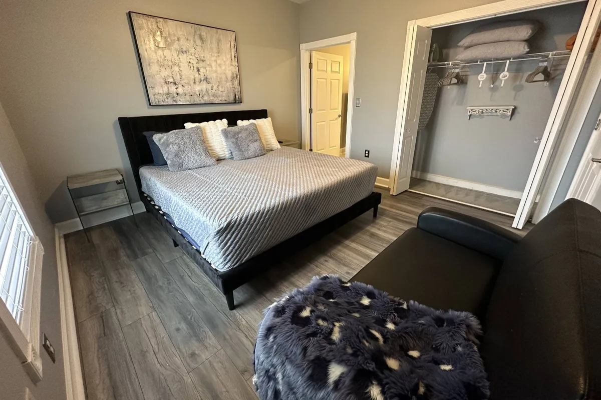 This image showcases a serene bedroom with a large bed, cozy sofa, artistic wall decor, and closet space. The atmosphere feels tranquil, inviting rest, reading, and personal relaxation. Morning light filters softly into the space, enhancing the sense of peace and privacy.
