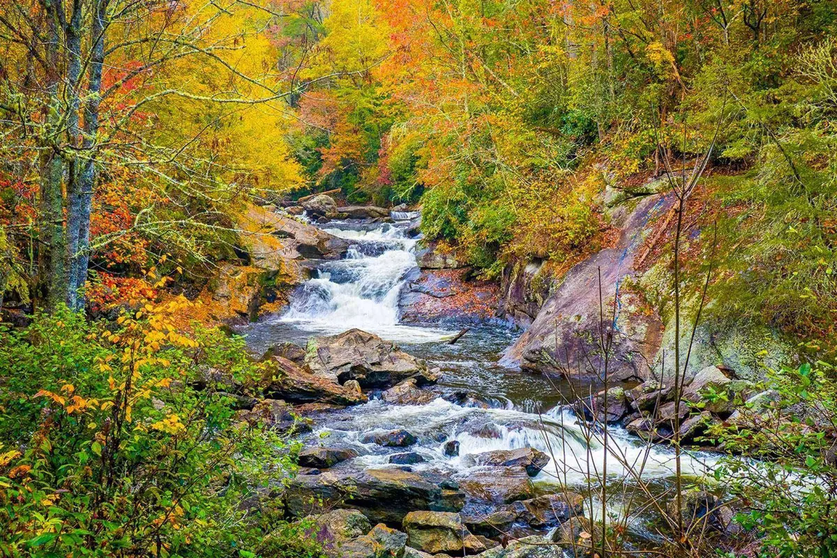 A scenic view featuring a flowing river surrounded by colorful foliage and striking rock formations. The natural beauty of the landscape invites calm reflection and relaxation, suggesting a peaceful environment outside the property.